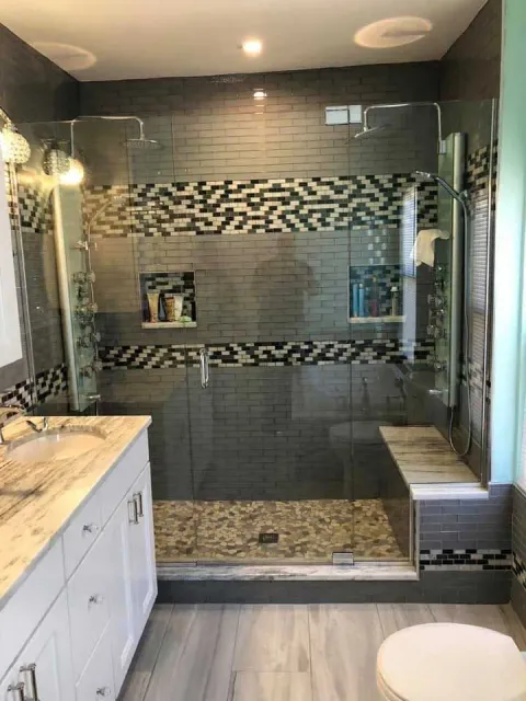 Modern bathroom with gray tile shower, glass doors, built-in bench, and white vanity.