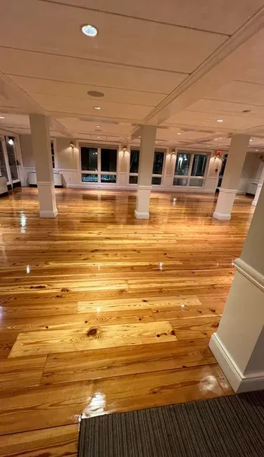 Spacious empty ballroom featuring polished heart pine hardwood floors, white support columns, and warm interior lighting.