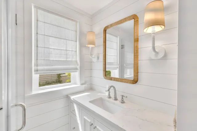 Bright white bathroom with vanity, mirror, window, and wall sconces