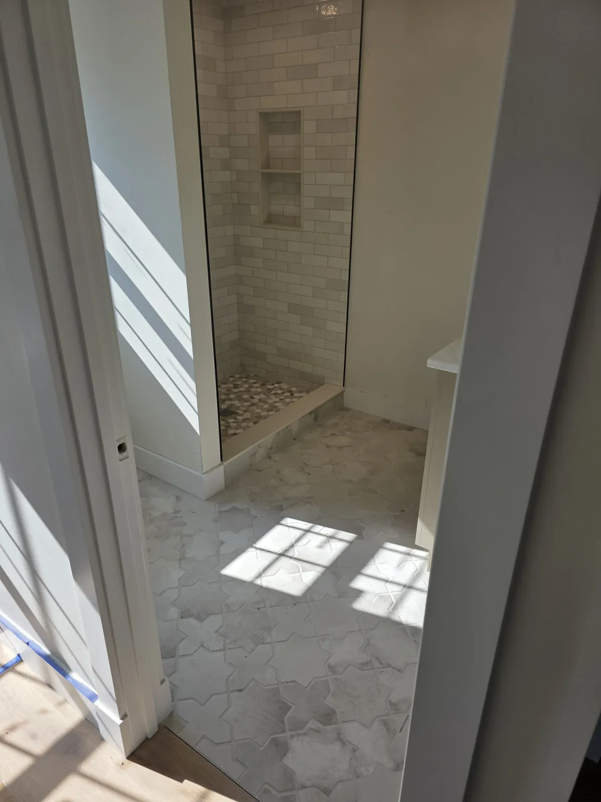 Wide view of an irregular-pattern tiled shower wall and niche