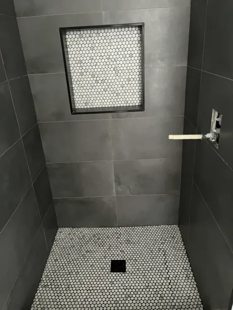 Shower in large charcoal tile with a penny mosaic niche and a matching penny mosaic floor