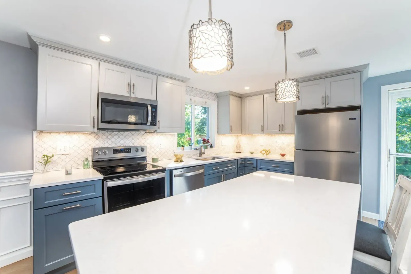 Bright modern kitchen with white island, gray cabinets, stainless appliances, and pendant lights