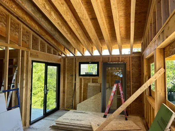Interior of a wood-framed room under construction with windows and exposed ceiling joists.