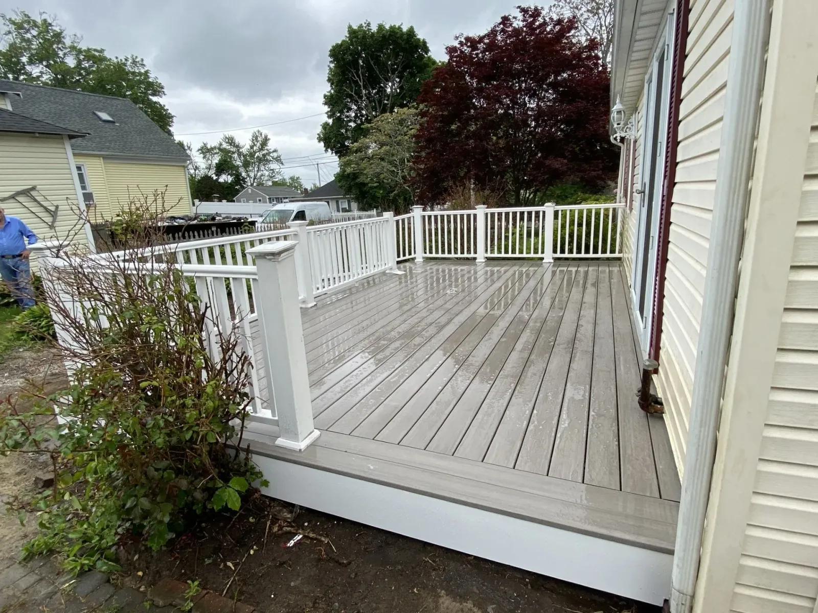 Small gray wooden deck with white railings beside a beige house on an overcast day