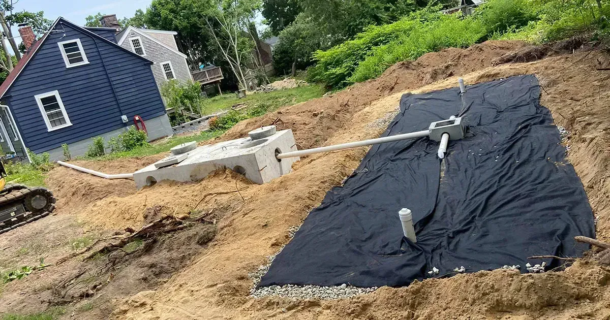 Construction site with a septic system installation. A blue house sits on a hill in the background.