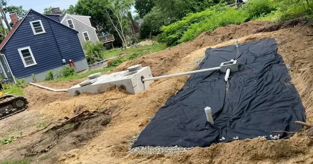 Construction site with a septic system installation. A blue house sits on a hill in the background.