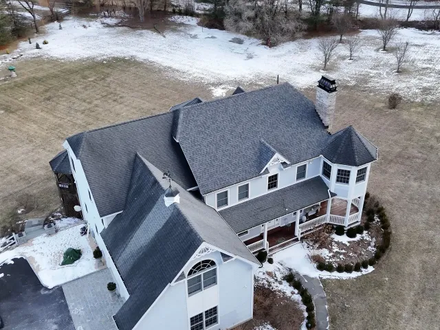 Aerial view of a large two-story house with dark gray roof, chimney, and snow-covered yard.