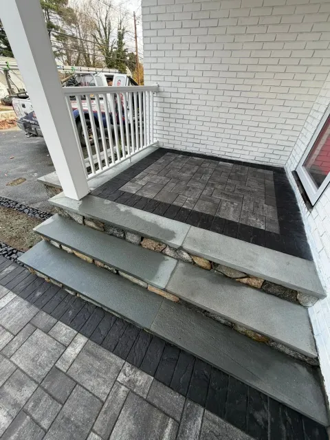 Front porch steps with a black landing mat and white railing beside a brick house