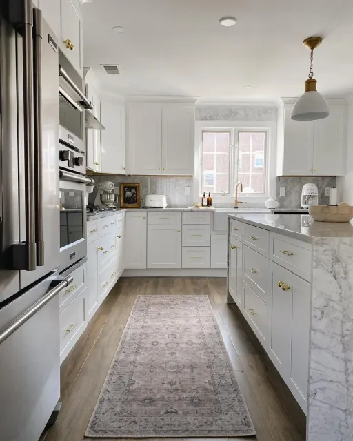 White kitchen with marble countertops, gold hardware, and a farmhouse sink, remodeled by Benchmark on the New Hampshire Seacoast