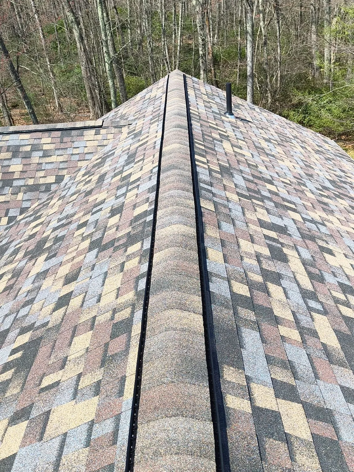 Roof with multicolored shingles and a central ridge, surrounded by trees.