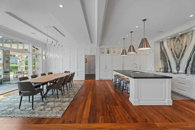 Spacious modern kitchen/dining room with wood floors, white cabinets, a long table, and island with bar stools.