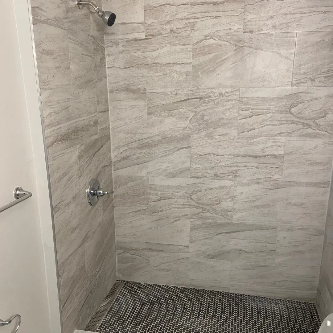 Stand-up tile shower with large-format gray stone walls and black hex floor by SF Construction in Framingham, MA