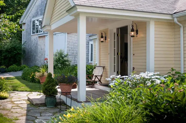 A porch with chairs and potted plants in the background.