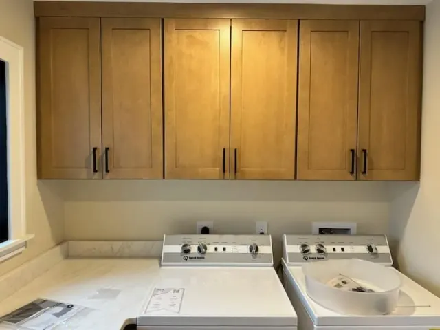 Light wood cabinets hang above a white washer and dryer in a laundry room.