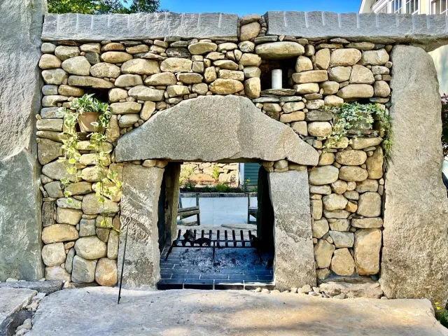 Rustic double-sided stone fireplace with granite posts, granite hearth, and built-in niches for plantings or decor in Easton, Connecticut.