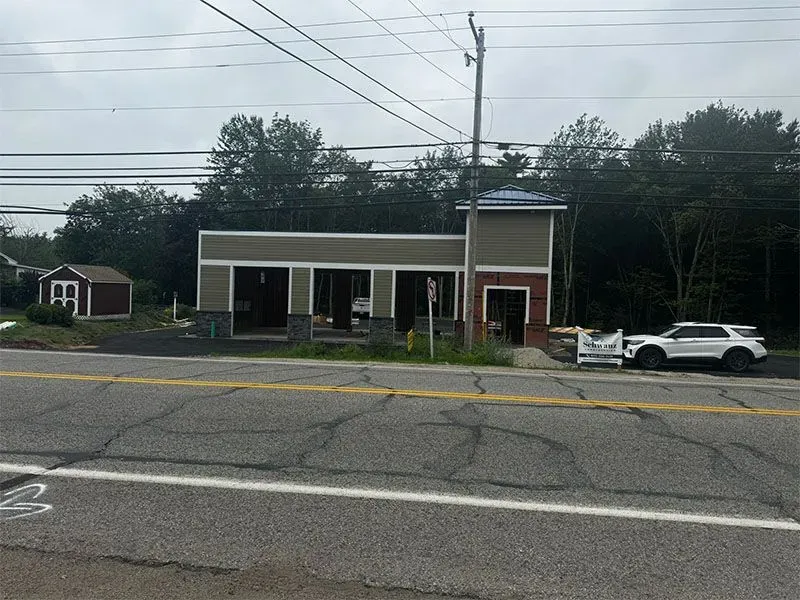 Building under construction with open bays on a road. A white SUV is parked in front.