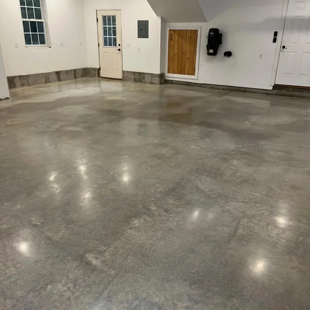 Empty garage with custom polished concrete floors, white walls, two windows, a door with a glass panel, a wooden door, an electrical panel, and a wall-mounted black device.