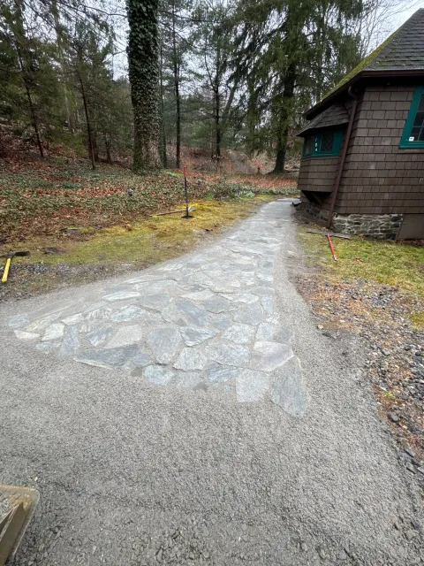 Gravel path beside a rustic cabin in a wooded area on a damp, overcast day