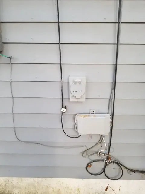Exterior house wall with electrical meter, utility boxes, and exposed cables.