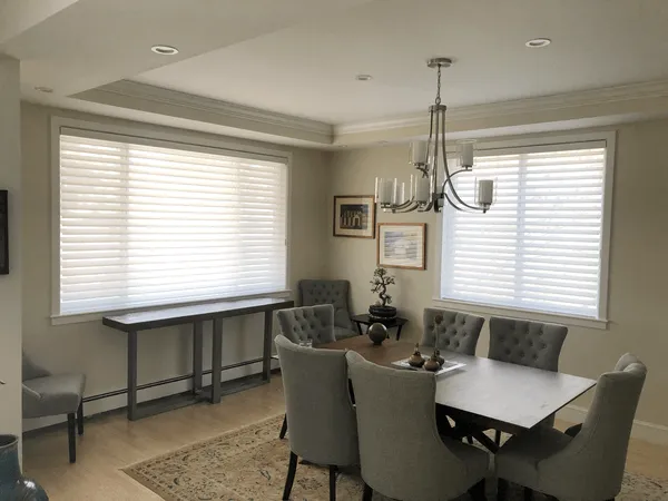 Dining room with two windows fitted with white silhouette shades, gray upholstered chairs around a dark wood table