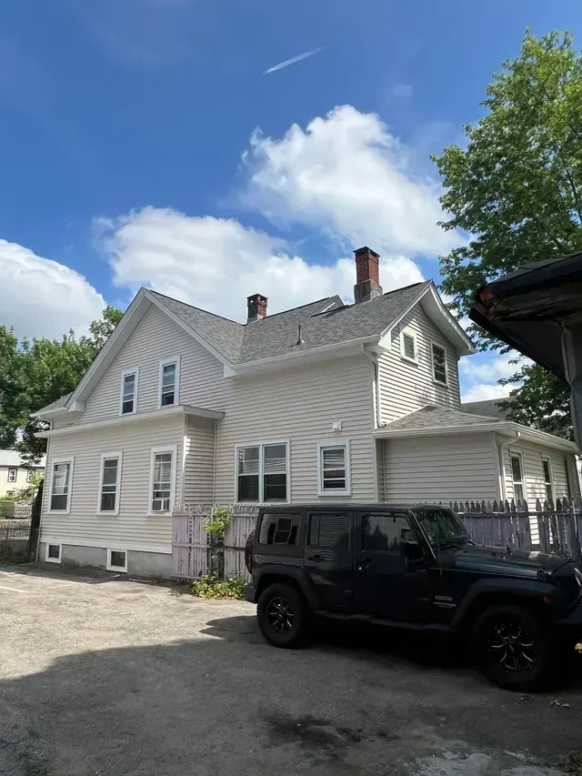White house with ornate trim under a blue sky, with a black Jeep parked in front