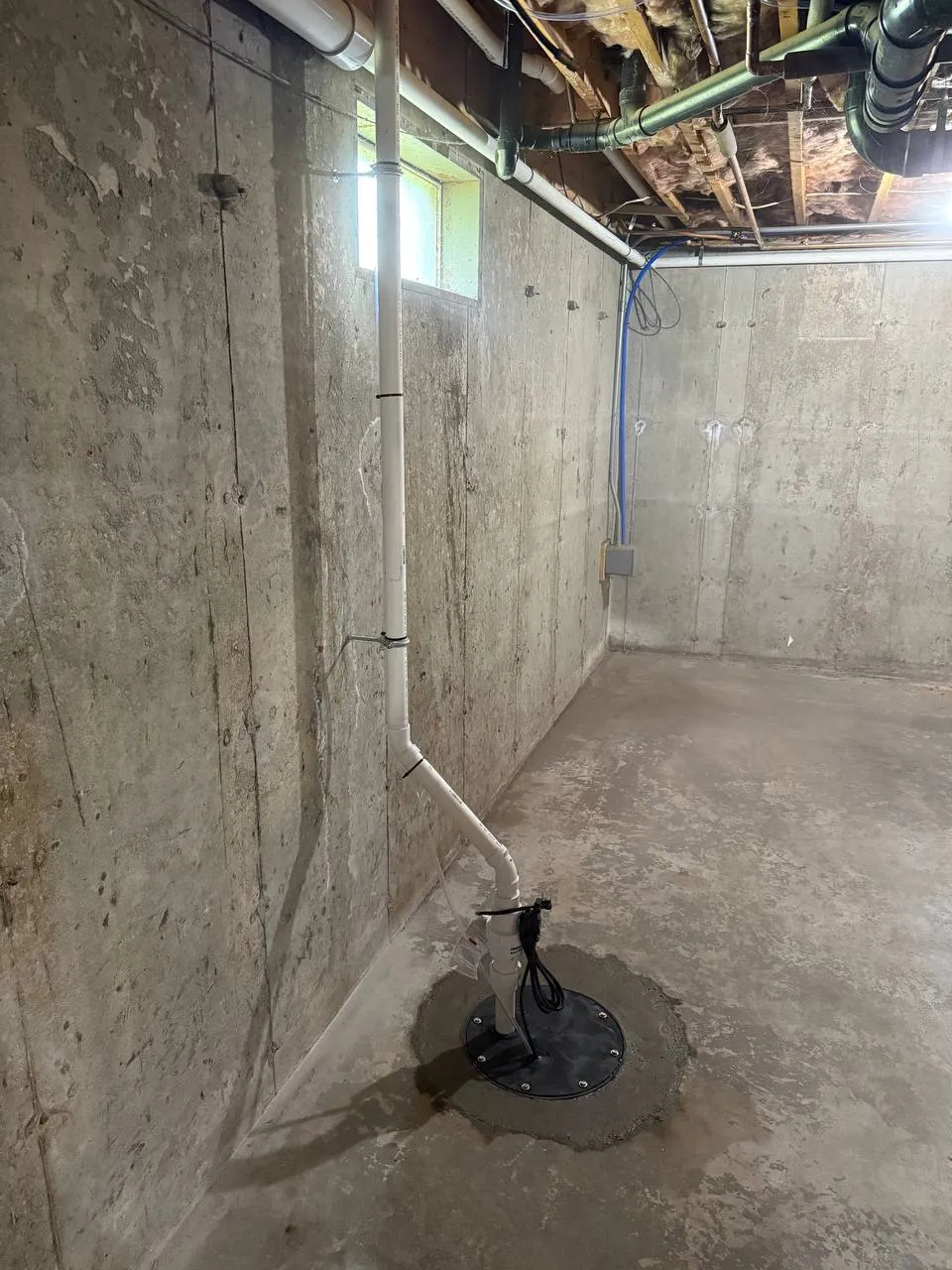 Sump pump with sealed basin lid and PVC discharge pipe in a concrete basement