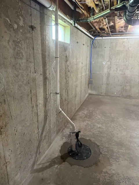 Sump pump with sealed basin lid and PVC discharge pipe in a concrete basement