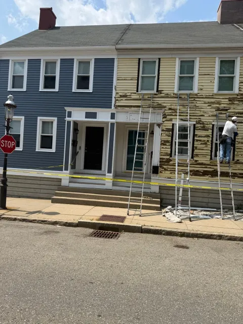 Row of townhouses with scaffolding and two workers painting the facade on a sunny street
