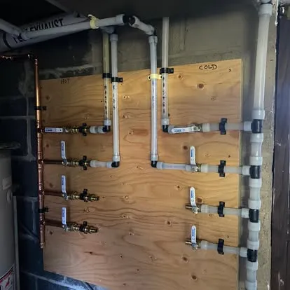 Plumbing manifold system with PEX and copper piping installed on plywood backing by Top Tier Plumbing & Heating LLC