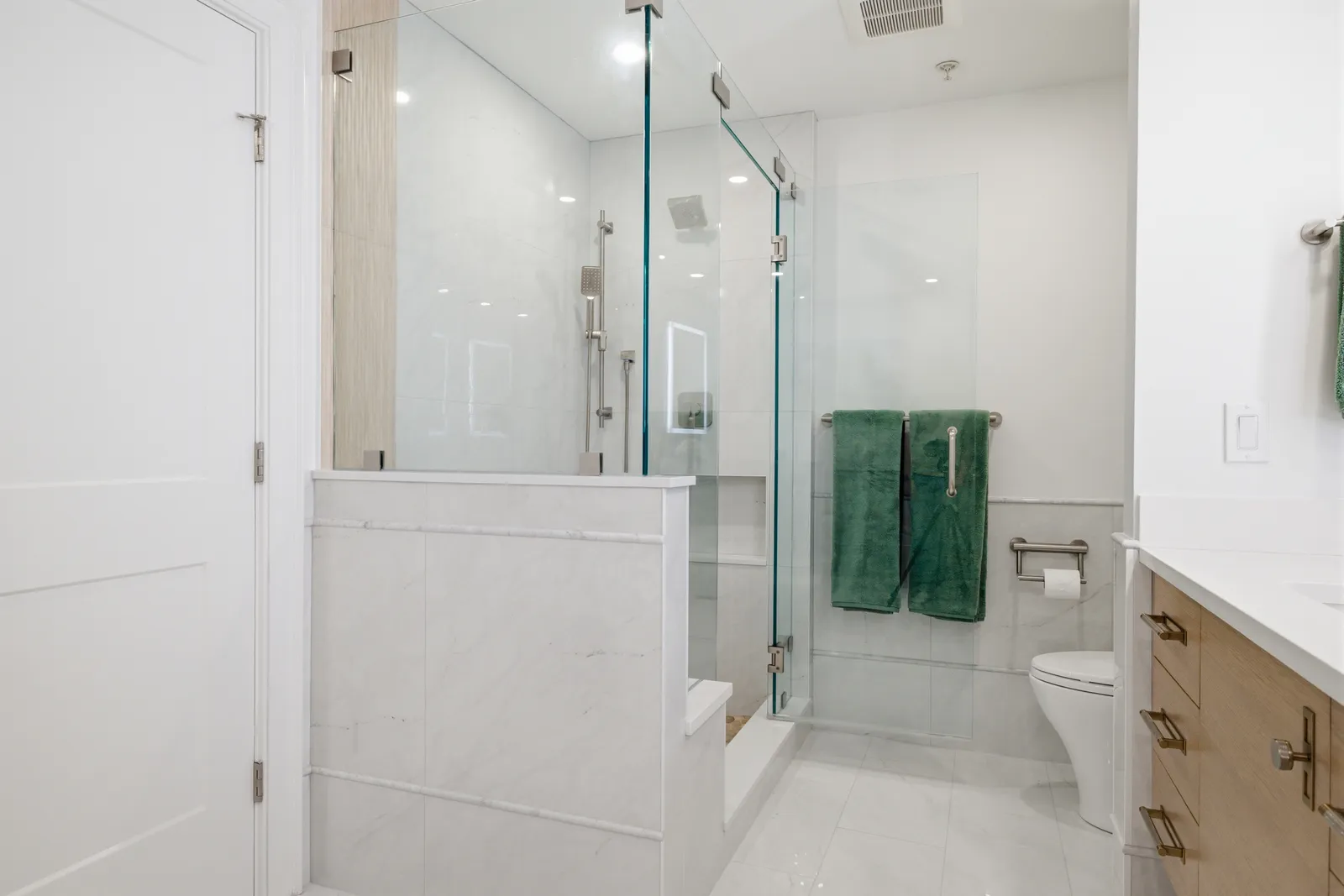 Walk-in glass shower with marble-look tile and a built-in half wall beside the toilet in a Braintree primary bath.