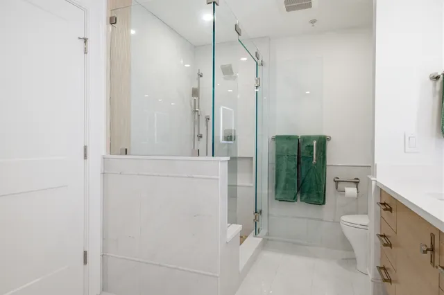 Walk-in glass shower with marble-look tile and a built-in half wall beside the toilet in a Braintree primary bath.