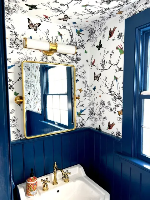 an elegant blue and gold bathroom with amazing wallpaper and a delightful sconce lighting fixture