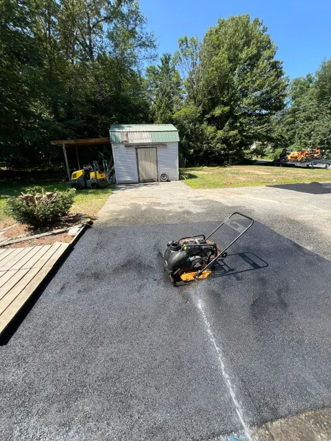 Asphalt paving, vibrating compactor on fresh blacktop driveway, shed in background.