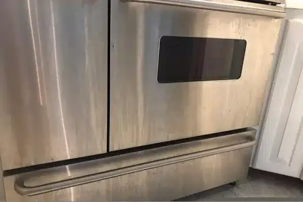 Stainless steel oven with a black window and a horizontal handle, adjacent to white cabinetry.