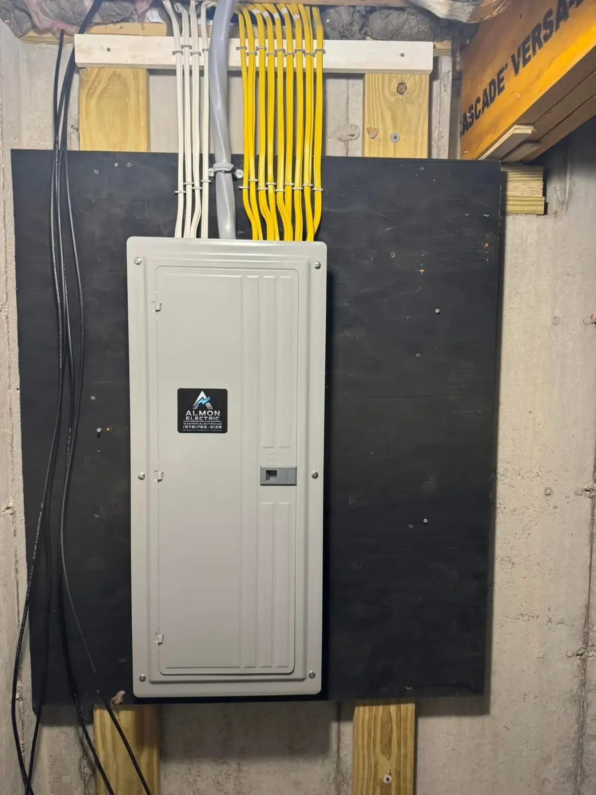 Electrical panel with various colored wires organized and attached to a black board on a concrete wall.