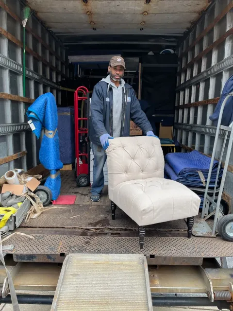 Mover unloading a cream tufted armchair from the back of a moving truck