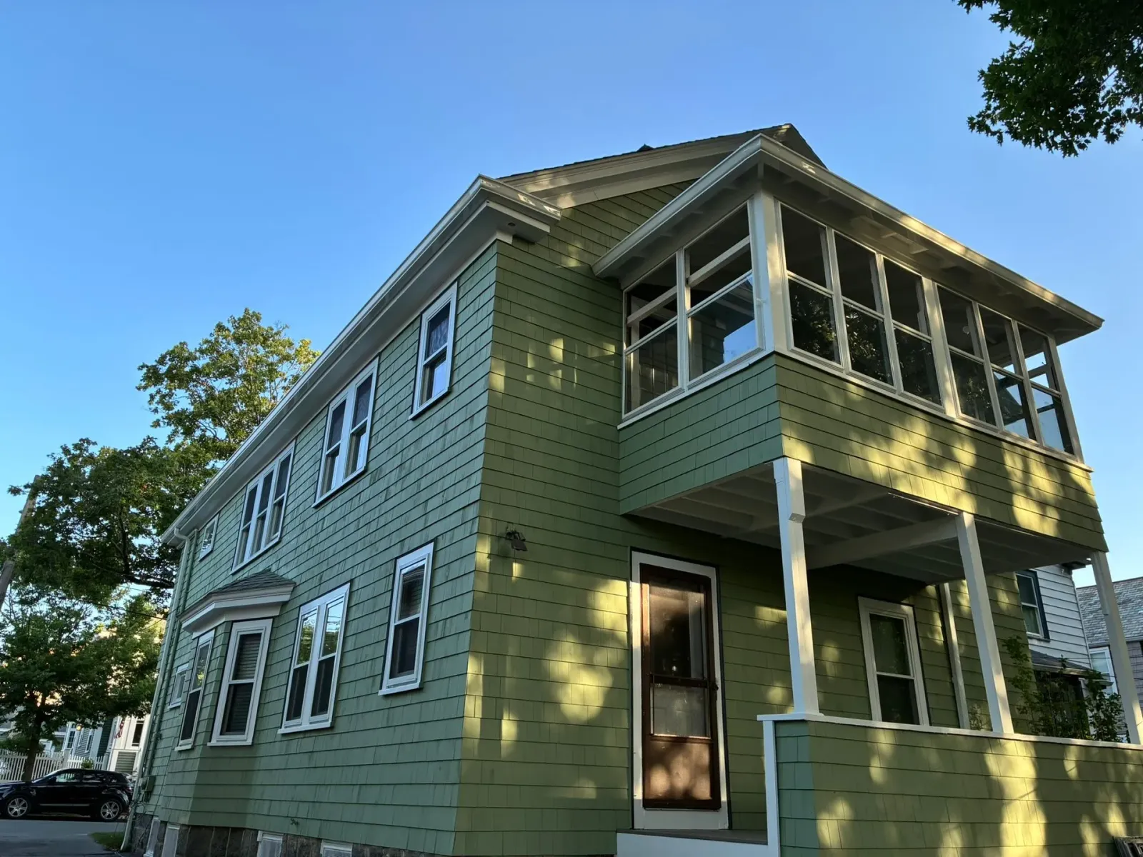 Green two-story house with a screened porch and white trim under a clear blue sky