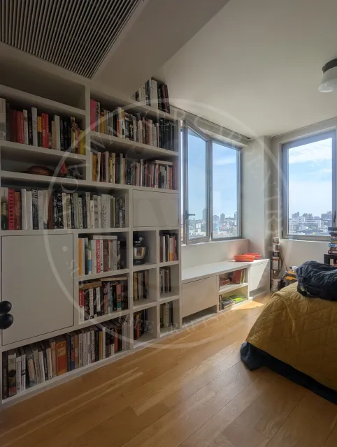 Custom floor-to-ceiling built-in bookshelves with integrated cabinet storage and a window bench, painted white and filled with books.