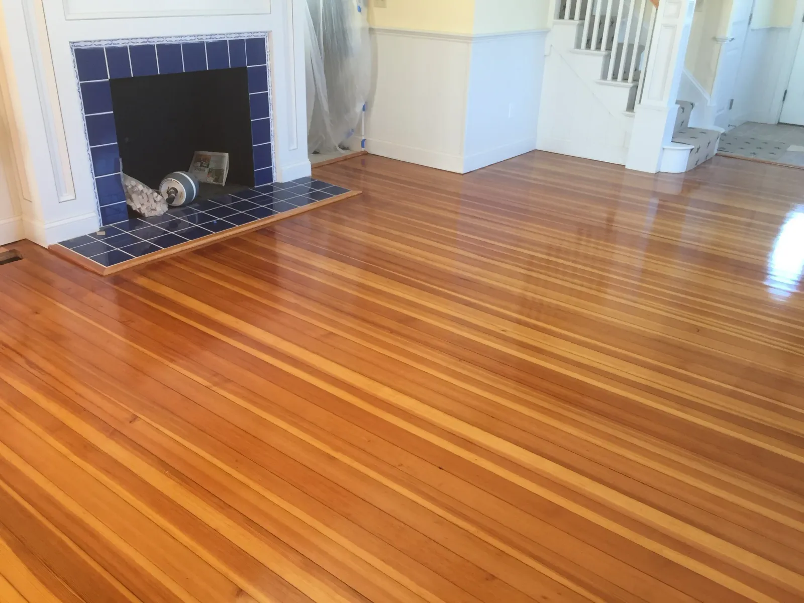 Living room with newly finished hardwood floors and a white fireplace with blue tiles.