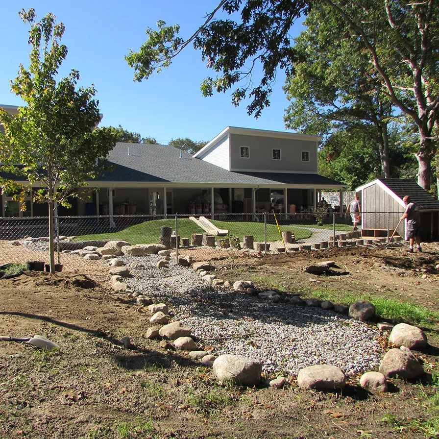 New gravel and rock landscape architecture design at preschool center. Person raking.