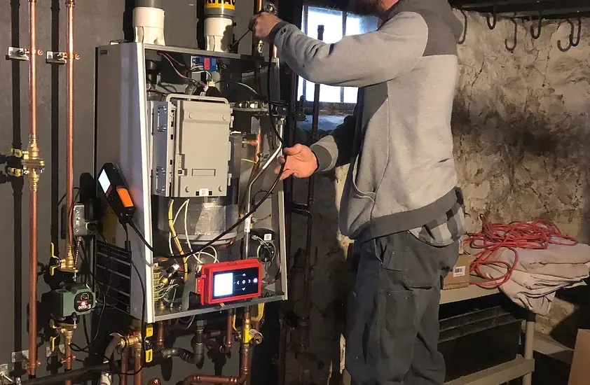 Technician working on an open HVAC unit with tools in a basement utility room