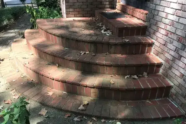 Before: Curved brick stairs leading up to a doorway, with scattered leaves on the steps and surrounding area.