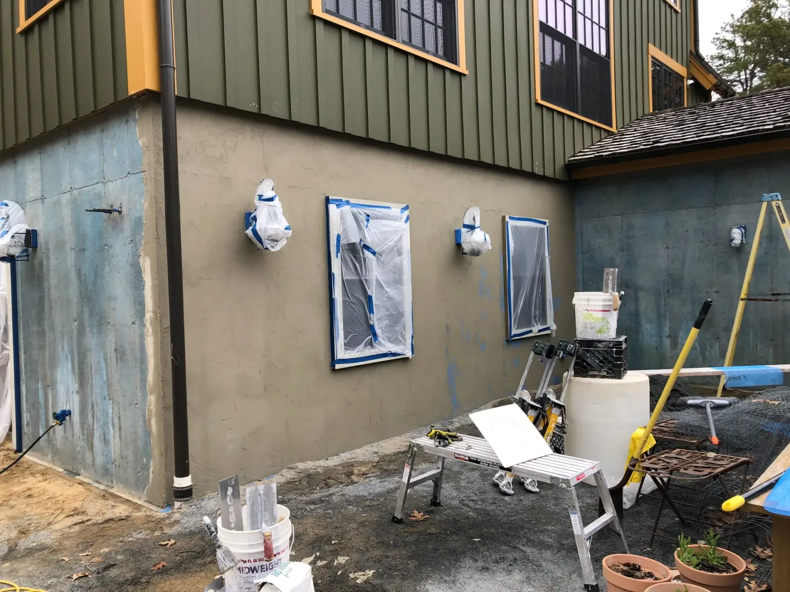 House exterior under renovation with tarped windows, tools, and construction materials in the yard