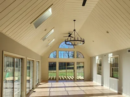 Bright sunroom with vaulted ceiling, skylights, chandelier, and large glass doors overlooking a lawn.