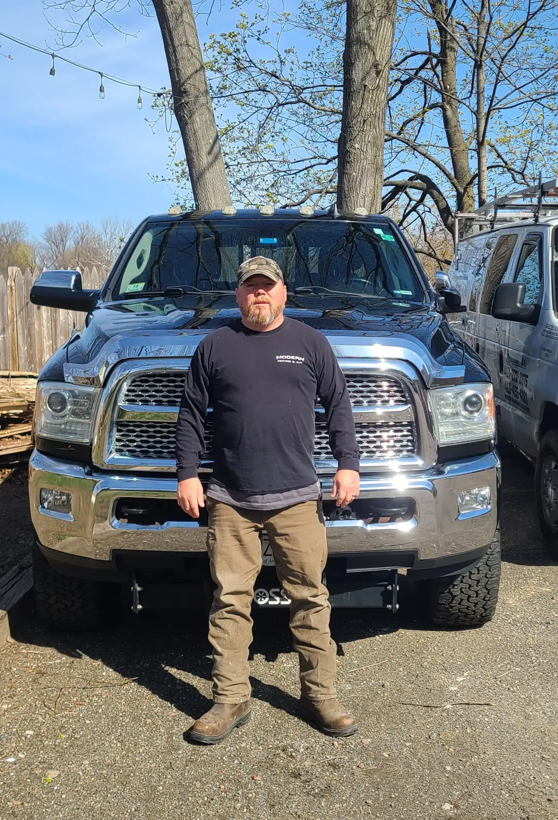 Person standing in front of a blue pickup truck on a gravel lot under a clear sky.