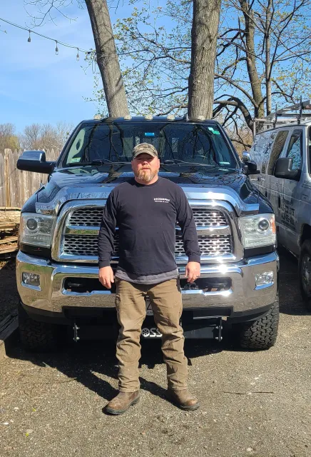 Person standing in front of a blue pickup truck on a gravel lot under a clear sky.