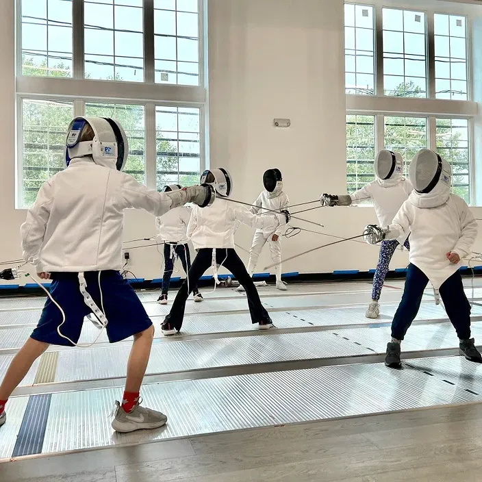 Children practicing épée fencing footwork and technique at Allez Fencing Club’s Learn to Fence class in Watertown, MA, inside a bright, modern training facility.