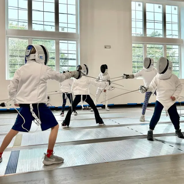 Children practicing épée fencing footwork and technique at Allez Fencing Club’s Learn to Fence class in Watertown, MA, inside a bright, modern training facility.