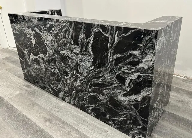 A black and white marble counter top is sitting on a wooden floor.
