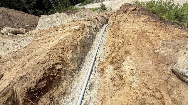 Open hillside trench with gray electrical conduit laid before backfill